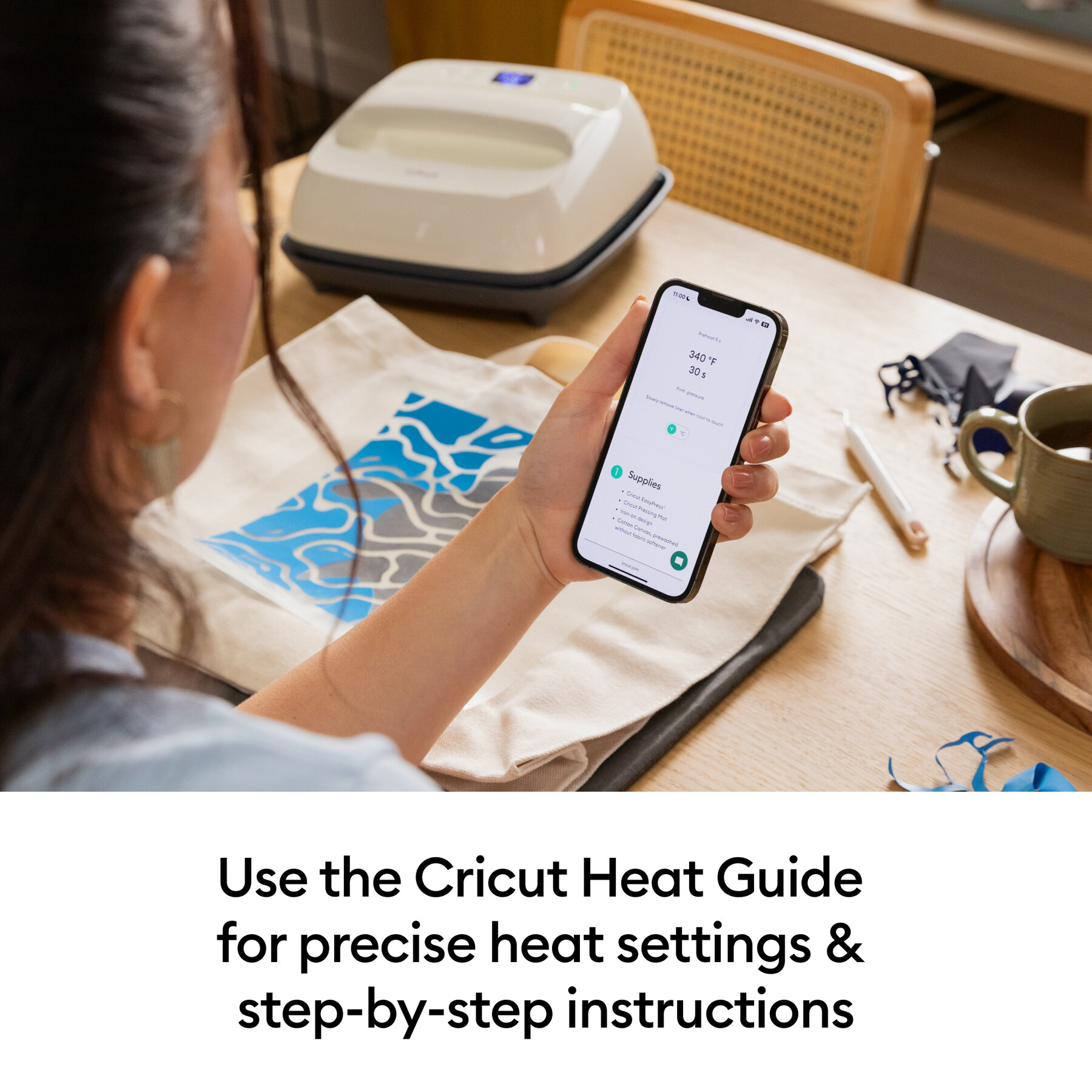 072012727infographic | Avloon Person holding a smartphone showing heat settings for Cricut while a compact heat press sits on a table nearby