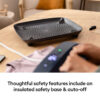 Black perforated safety tray on a wooden table with a hand operating a nearby control device in the foreground