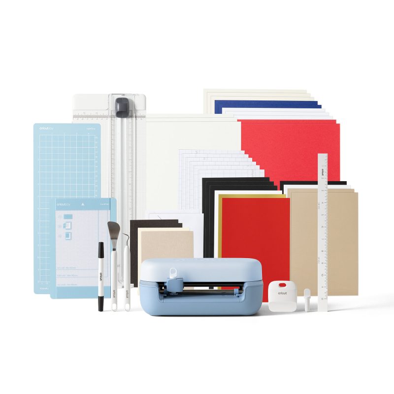 Cricut cutting machine with assorted colored paper packs, mats, rulers, and craft tools on a white background.